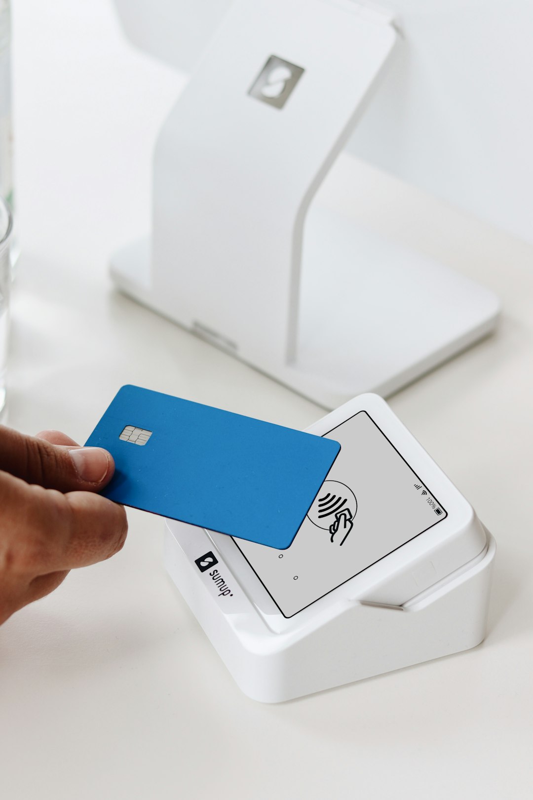 A close-up of a customer making a contactless payment with a blue card using the SumUp Solo card reader. In the background, a larger point of sale (POS) system is visible, emphasizing the versatility and modern design of SumUp's payment solutions. The scene reflects a sleek and efficient checkout process ideal for small businesses, beauty salons, cafes, or retail environments.